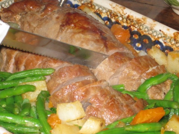 Stepmom slicing terriyaki pork tenderloin (flanked by sweet potatoes, white potatoes, carrots, and green beans)